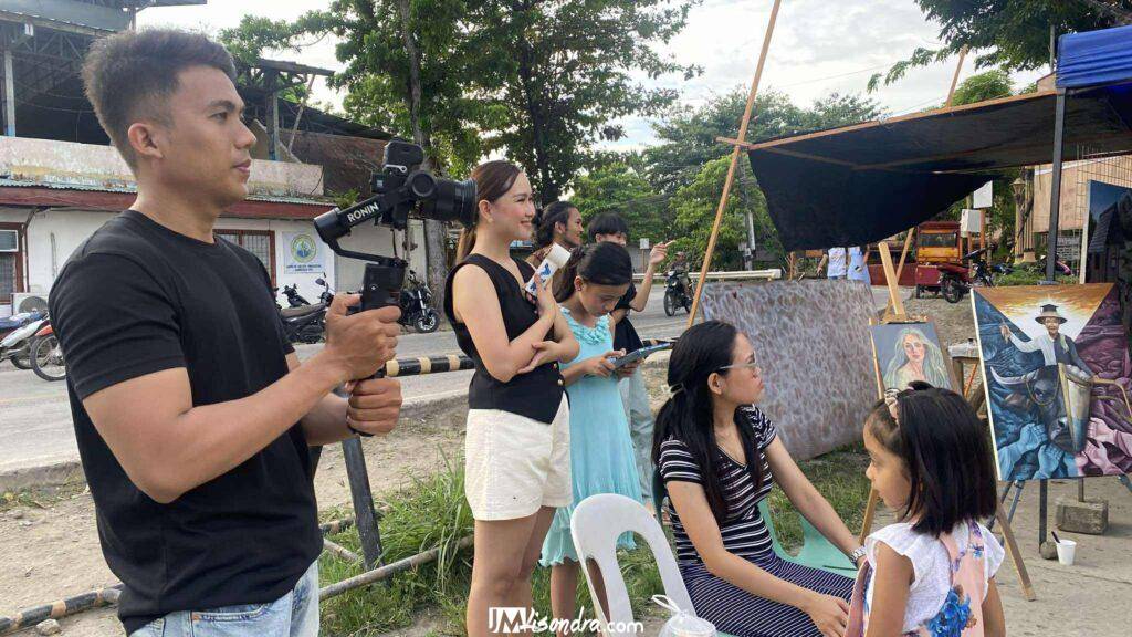 Ringing in a New Era: Guihulngan Kampana Artists Ignite the Local Art Scene with "PintaPasiugda"! 32 a man holding a camera and a group of people